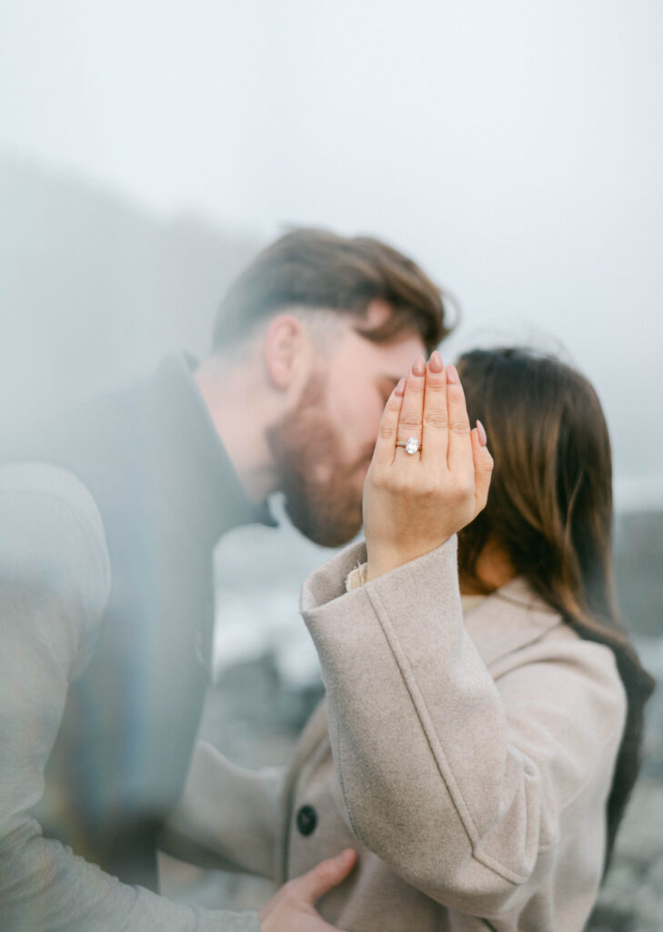 Engaged couple kissing on rocks at cliff house Maine in winter